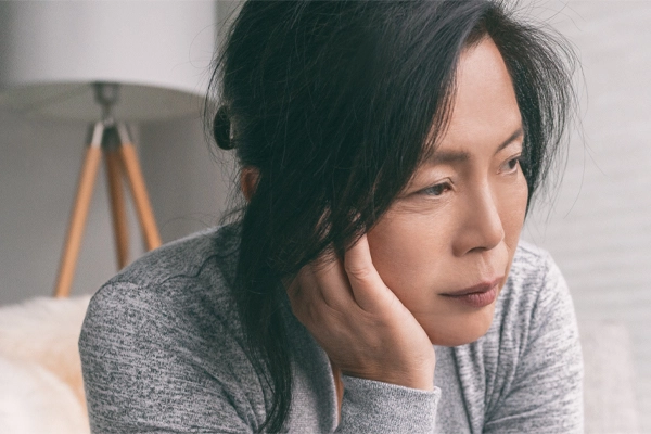 Adrenal-Fatigue-Doctor A middle-aged asian woman sitting on her couch, resting her head on her hand, suffering from adrenal fatigue. Get treatment for adrenal fatigue syndrome from AZENA Health & Longevity in Gainesville.