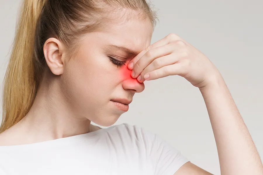 Allergic-Rhinitis-Clinic A woman grimaces and rubs the bridge of her nose due to sinus irritation. Get treatment for allergic rhinitis from AZENA Health & Longevity in Gainesville.