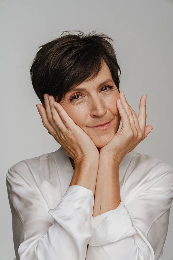 Angioedema-Treatment A middle-aged woman with short brown hair touches her face after successful angioedema treatment from AZENA Health & Longevity in Gainesville.