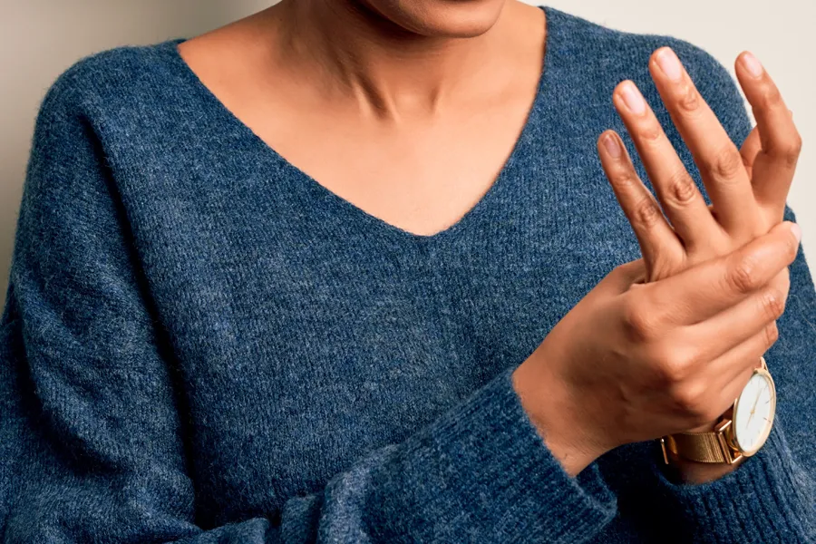 Arthritis-Doctor Close up of a woman in a blue sweater massaging one aching hand with the other. Get help for arthritis from AZENA Health & Longevity in Gainesville.