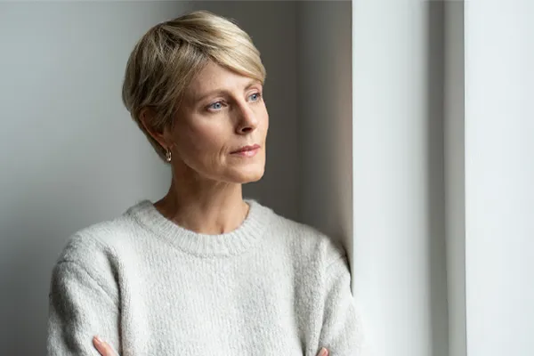 Chronic-Fatigue-Therapy A blond, middle-aged woman looks out the window with a tired expression. Get chronic fatigue treatment from AZENA Health & Longevity in Gainesville.