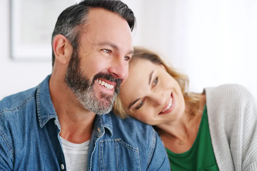 A middle-aged white couple in a bright white room smile and lay their heads on each other. Schedule concierge health and wellness services from AZENA Health & Longevity in Gainesville.