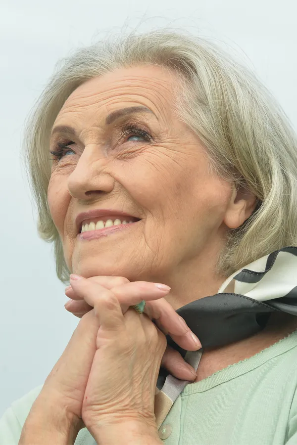 Hot-Flashes-and-Night-Sweats-Treatments An older woman holds her hands together under her chin and looks up at a cool sky smiling. Get treatment for hot flashes and night sweats from AZENA Health & Longevity in Gainesville.