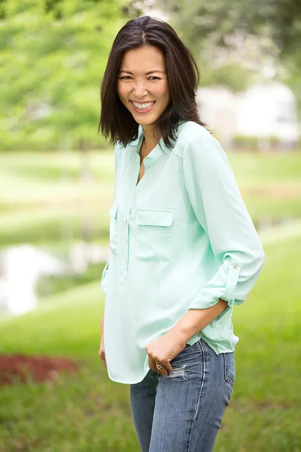 Perimenopause-Treatment A middle-aged brunette woman in a light green button-up shirt stands outside smiling, happy with her perimenopause treatment from AZENA Health & Longevity in Gainesville.