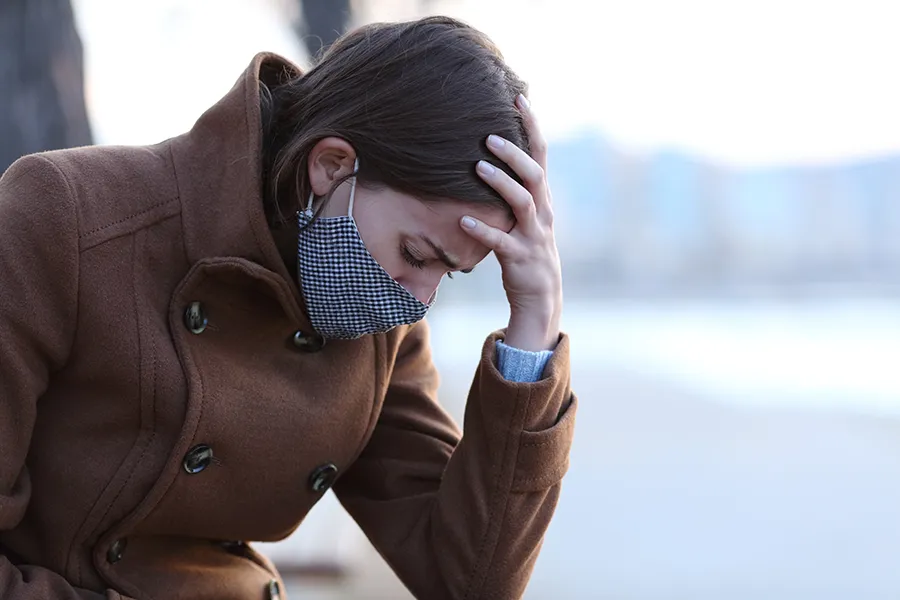 Post-Covid-Clinic A woman in a mask sits outside with her hand on her forehead in pain. Get long covid treatment from AZENA Health & Longevity in Gainesville.