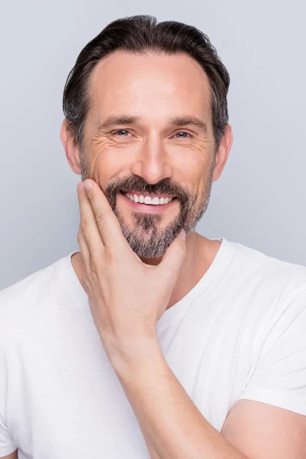 Sjogrens-Syndrome-Treatment A middle-aged bearded man touches his smiling face. Get treatment for Sjogrens Syndrome from AZENA Health & Longevity in Gainesville.
